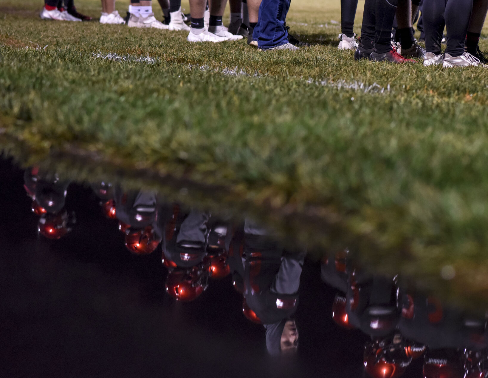 Southern Boone High School football players are reflected in a stagnant pool of rainwater as they stand on their home sidelines